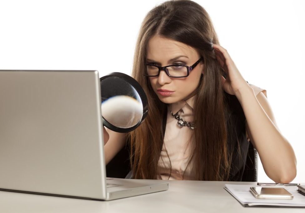 beautiful business woman looking through the magnifying glass at her laptop